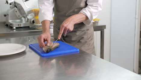 male cook fillets raw fish with knife in kitchen, medium pan shot