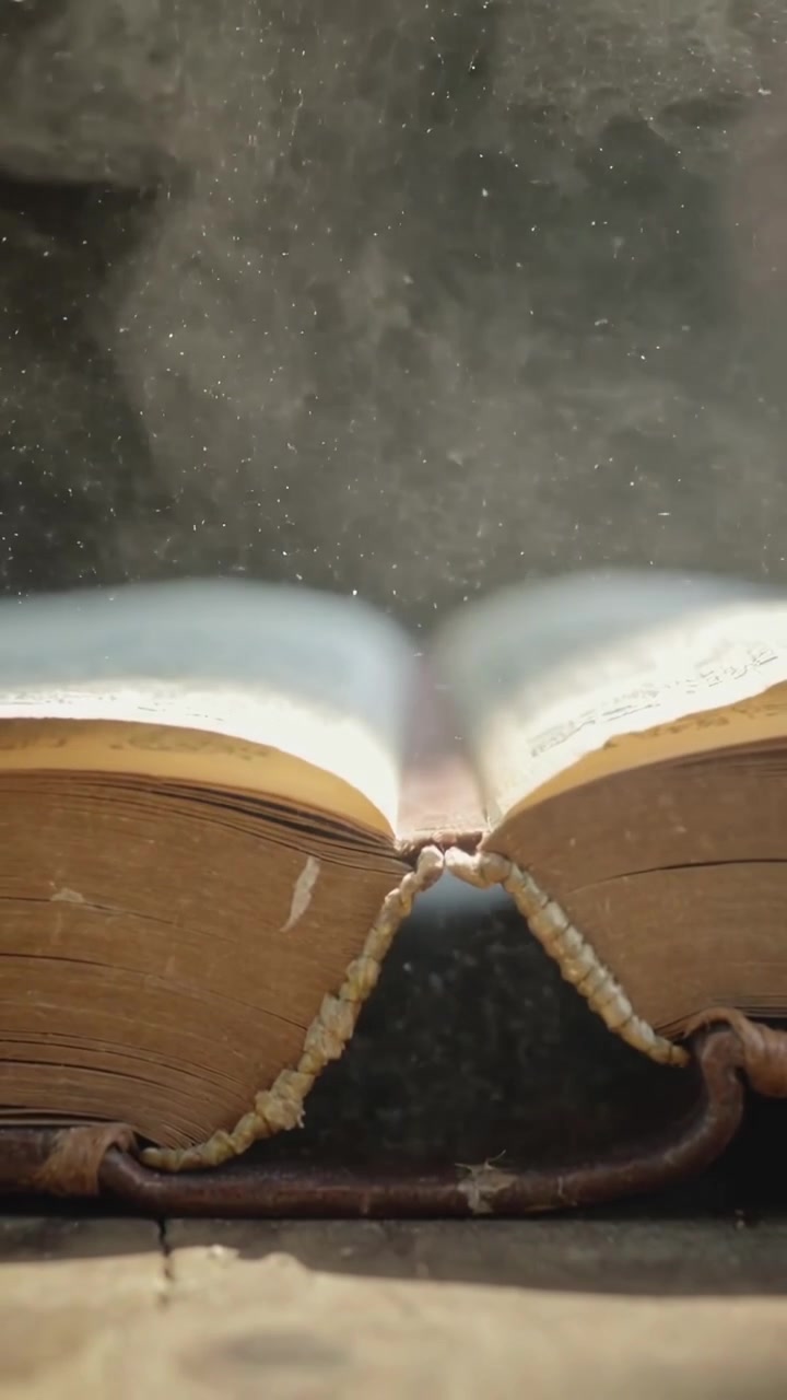 Verticale video: Pagina's van een oud leren boek gaan open, stof komt vrij uit de rug op een houten tafel in het licht.