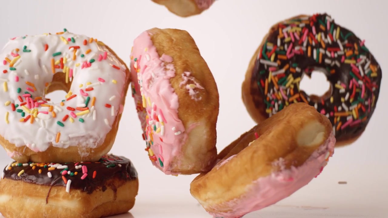 Ciambelle colorate con granella che rimbalzano e rotolano su uno sfondo bianco in una ripresa macro da studio al rallentatore. Video per feste di compleanno per bambini, contenuti per celebrazioni, post per feste festive