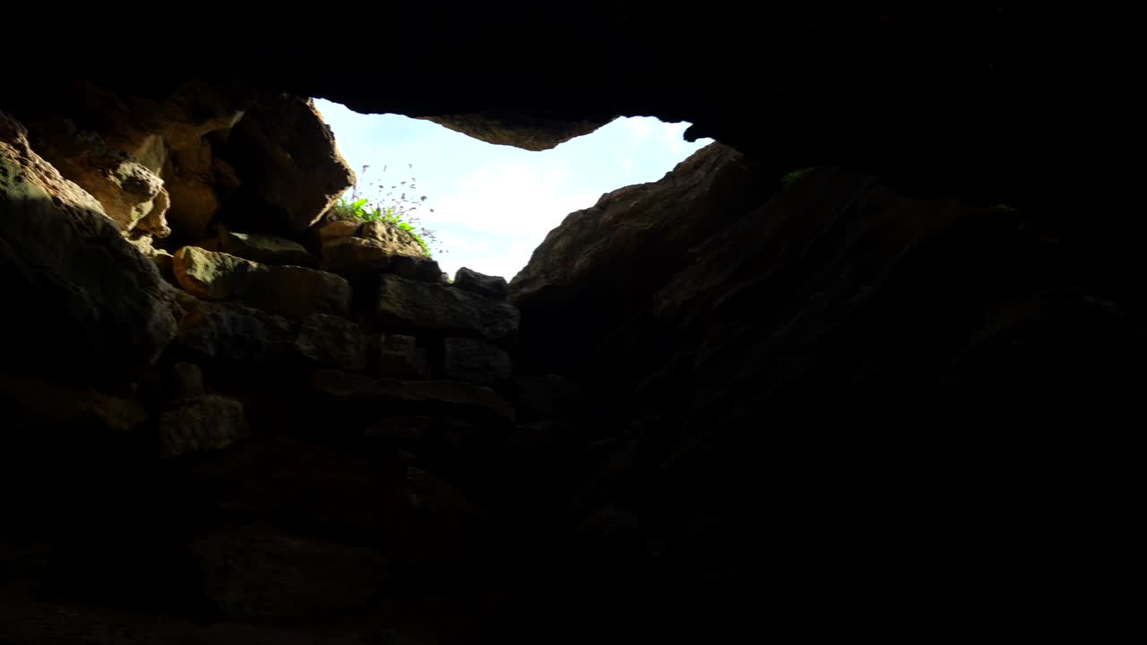Looking up from within Cucabrera Cave in Cantabria, blue sky visible through rock fissure, slow-motion pan