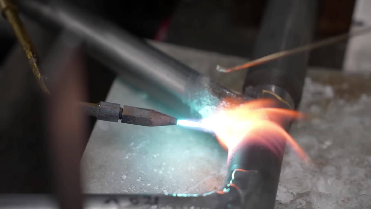 Extreme close up of a bright blue blowtorch flame heating a metal joint during a precision brazing process on a bicycle frame