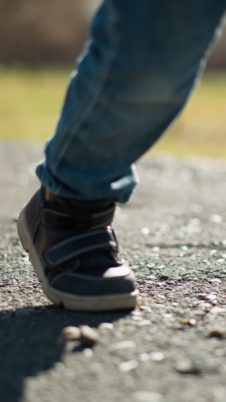 un primer plano de un adulto y un niño con vaqueros y botas caminando por un pavimento, sus sombras se reflejan en el suelo, y el pavimento muestra un pequeño agujero