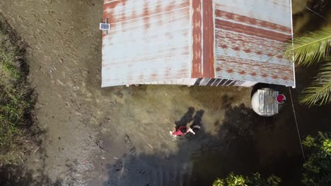 aerial top down shot showing woman and daughter leaving flooded homestead in cambodia