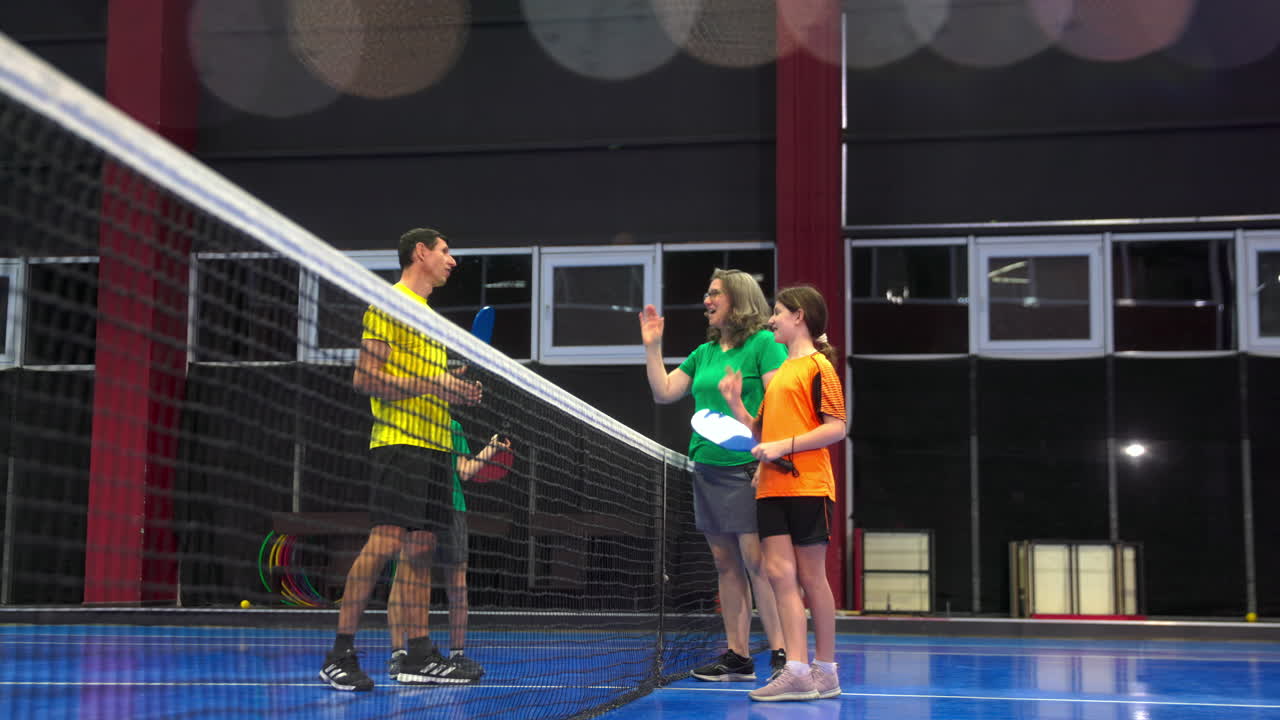 Two adults and two children high-fiving after playing pickleball on a blue, inside court