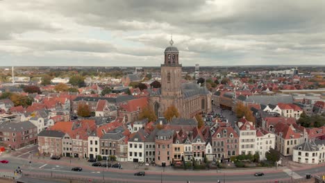 aerial drone shot starting high up and slowly descending showing the dutch medieval city of deventer revealing the boulevard with traffic at the river ijssel that passes by on a cloudy day