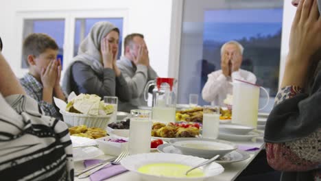 muslim family praying before having iftar dinner together during a ramadan feast at home