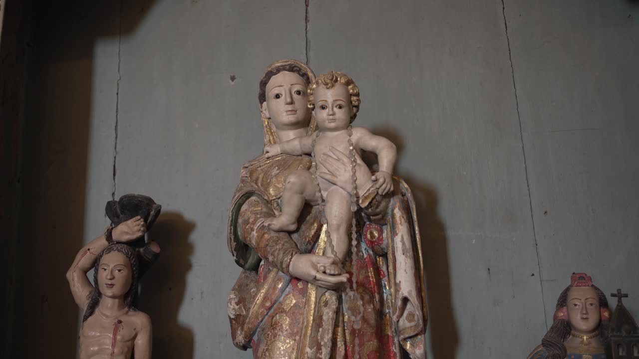 wooden statue depicting a serene Madonna holding a child, with other smaller statues in the background