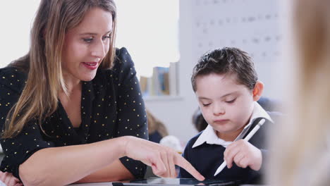 Female-teacher-working-with-a-Down-Syndrome-boy-using-tablet-in-primary-school,-front-view,-close-up