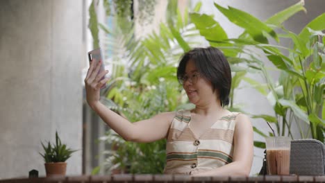 female tourist short hair wearing glasses sitting in greeting too smartphone family and having fun selfies in coffee shop. women feel relaxed and happy long weekend activities.