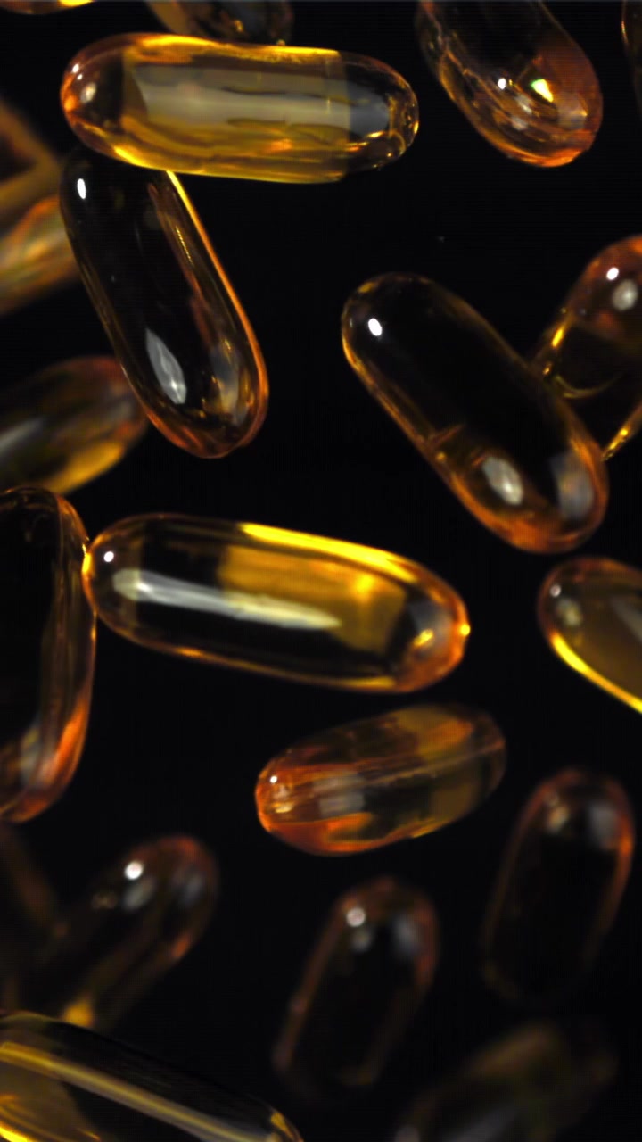 Capsule di Omega 3 dorate che galleggiano su sfondo scuro
