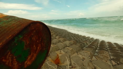 marine pollution concept, waste rusty can laid on tropical beach with seascape pristine water crashing on rocks