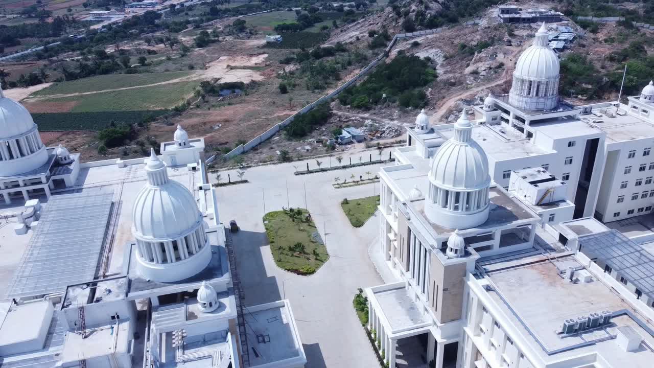 Aerial drone pulls back over the rooftops of a grand building with multiple white domes. Revealing shot of a new university or hospital campus