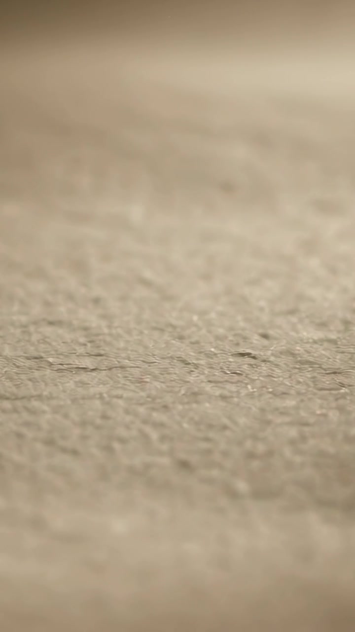 Vertical video: Pulling focus camera showing fibrous beige surface on tabletop, revealing warm band
