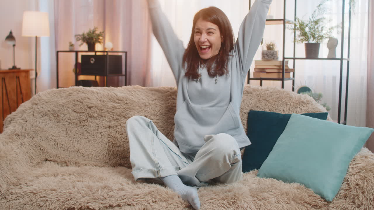 Woman on sofa using smartphone happily jumping and shouting with joy celebrating victory in game