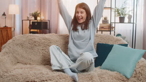 woman on sofa using smartphone happily jumping and shouting with joy celebrating victory in game