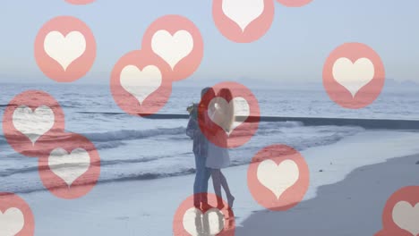 Multiple-red-heart-icons-floating-against-caucasian-couple-kissing-on-the-beach