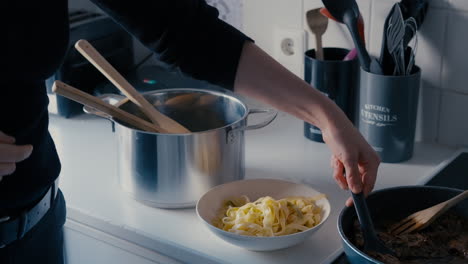 Mujer-Joven-Poniendo-Salsa-De-Carne-De-La-Sartén-Sobre-La-Pasta-Tagliatelle-En-Un-Plato-En-La-Cocina-Blanca-Durante-Un-Día-En-Cámara-Lenta