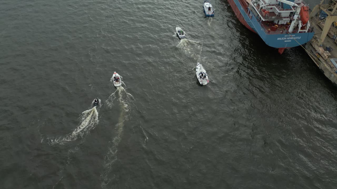 Boats sailing on dark water in sync creating trails seen from an aerial view