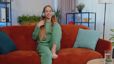 chica feliz y relajada con auriculares inalámbricos bailando escuchando su música rock n roll favorita en el sofá de casa