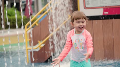 adorable toddler girl reaching out to touch fountain water sprayed at outdoor playground