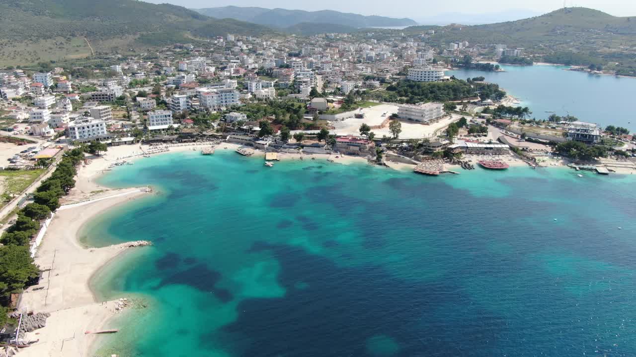 Drone view in Albania flying over white sand beaches, blue crystal clear water, hotels, sunny day in Ksamil