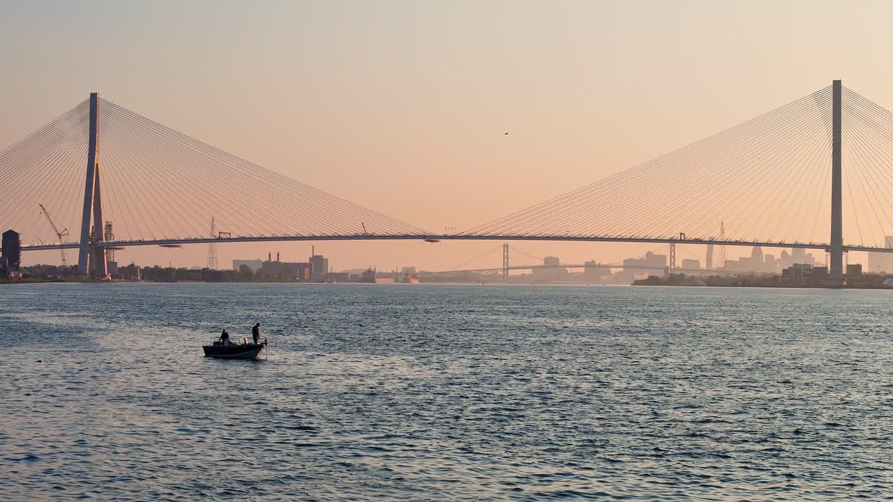 Gordie Howe International Bridge over Detroit River at sunset with city skyline view and fishing boat