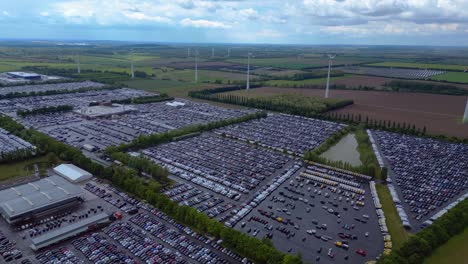 large parking lot full of cars near a wind farm and countryside in germany. wonderful aerial view flight panorama orbit drone