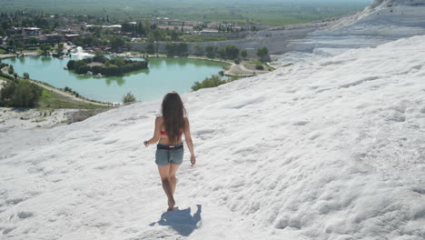 rückansicht einer jungen frau, die barfuß auf weißen travertinen von pamukkale, türkei, zeitlupe läuft