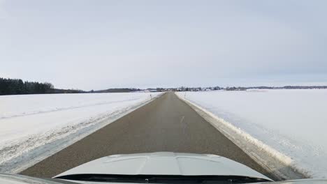 conduciendo a través de un paisaje nevado a lo largo de una carretera recta en coche a la vista del parabrisas en un frío día de invierno