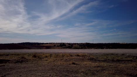 A-motion-lapse-moving-slowy-to-the-right-of-a-straight-dirt-road-under-a-light-cloudy-sky