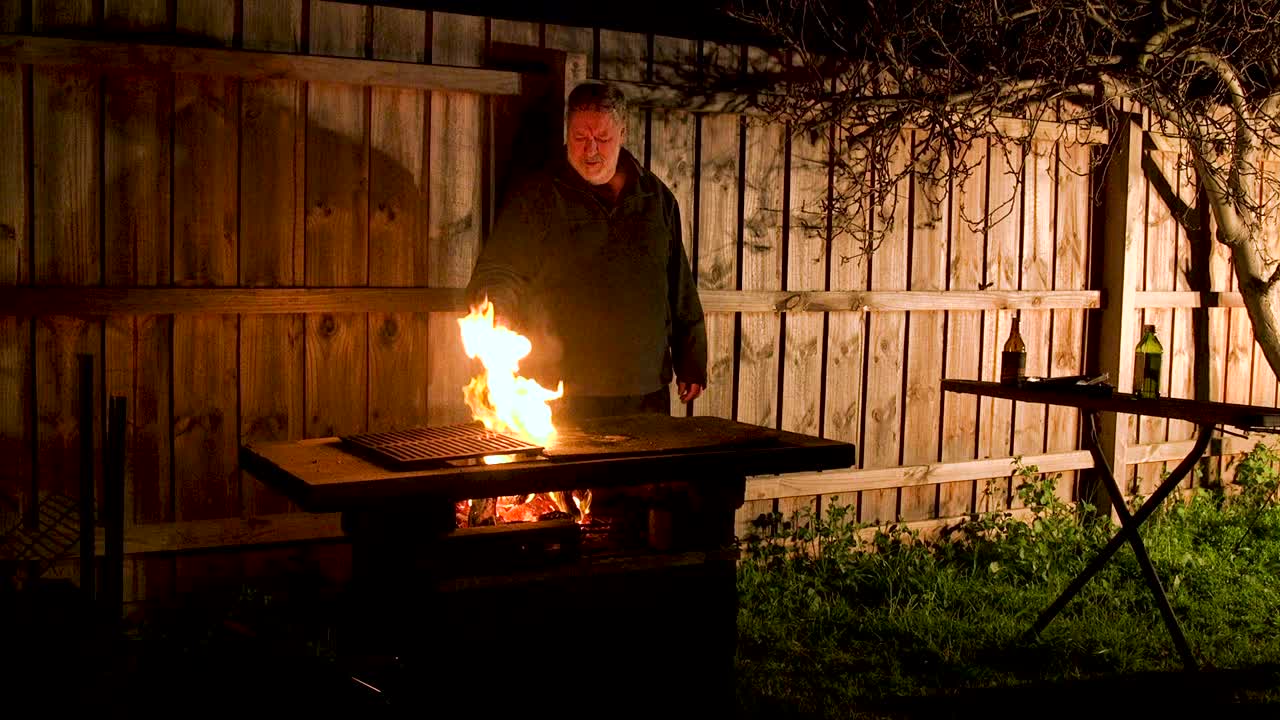 바비큐에서 남성이 요리하고 기름이 타서 요리사를 깜짝 놀라게 합니다.