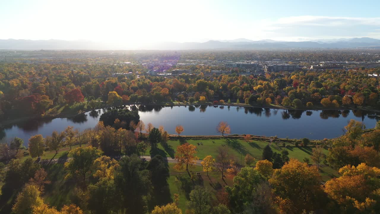 콜로라도주 덴버를 배경으로 호수 물과 산맥을 통해 햇빛이 비치는 워시 파크의 웅장한 가을 풍경을 타고 걷는 사람들