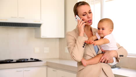 businesswoman holding baby while talking on the phone