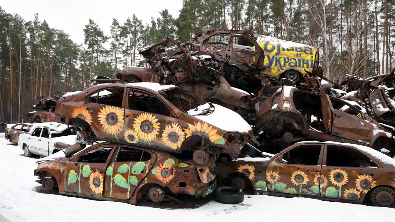 A winter day in Irpin, Ukraine, reveals a pile of charred and destroyed cars, with several vehicles painted with sunflower drawings, after fierce battles between Ukrainian and Russian forces.