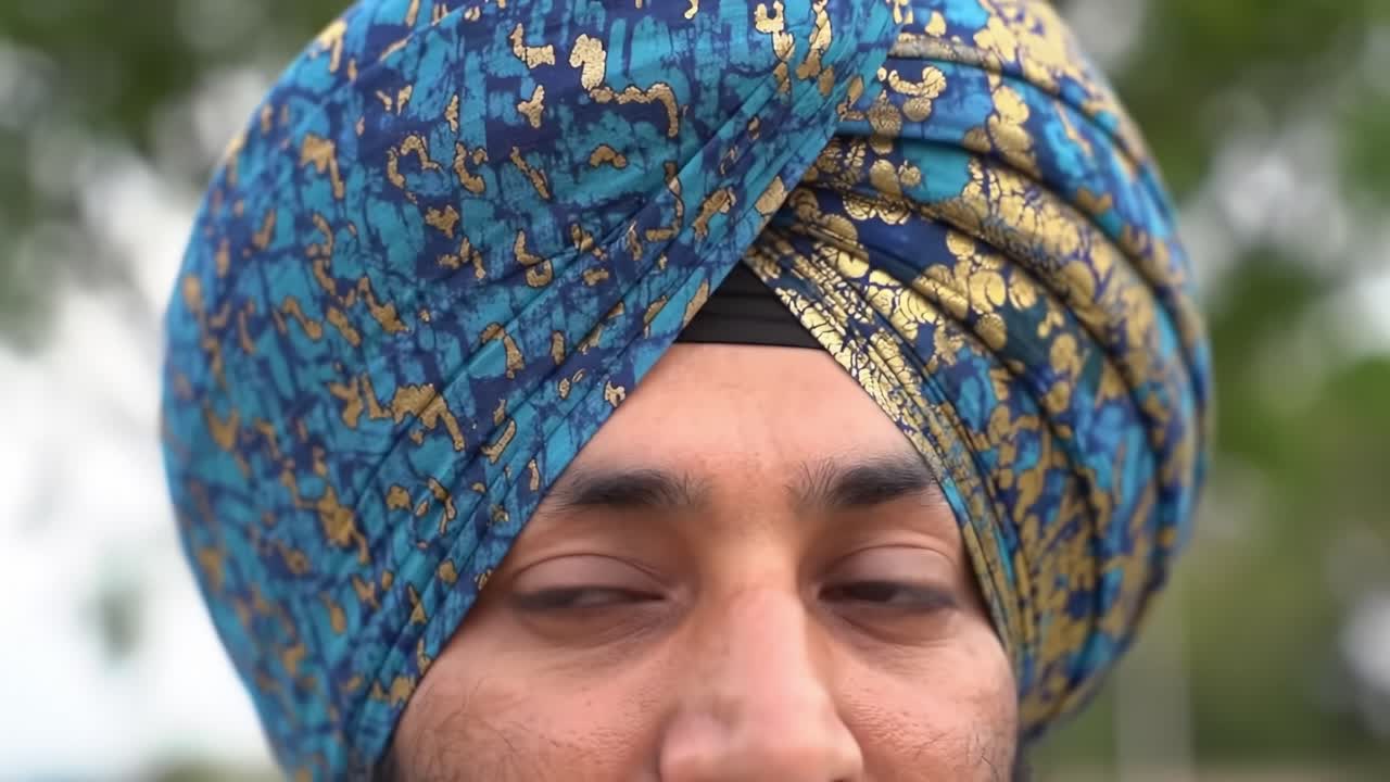 A man proudly wears a colorful turban with intricate patterns during a lively outdoor event. The scene captures the spirit of celebration and cultural pride in a natural environment.