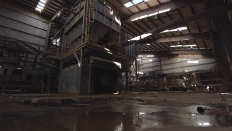 slider footage of machinery in an abandoned brick factory with a puddle in the foreground, shale storage, graffiti, decay, conveyor belts