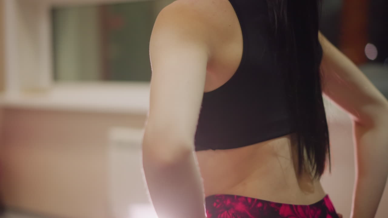 Donna si allunga con sicurezza in leggings rosa e top sportivo, silhouette della coda di cavallo, schiena e addome tonici. Illuminazione calda dello studio e palla fitness sullo sfondo, alla fine di una sessione di allenamento concentrata.