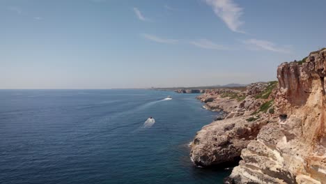 aerial: drone flying beside cliffs of mallorca coastline with boats in summer