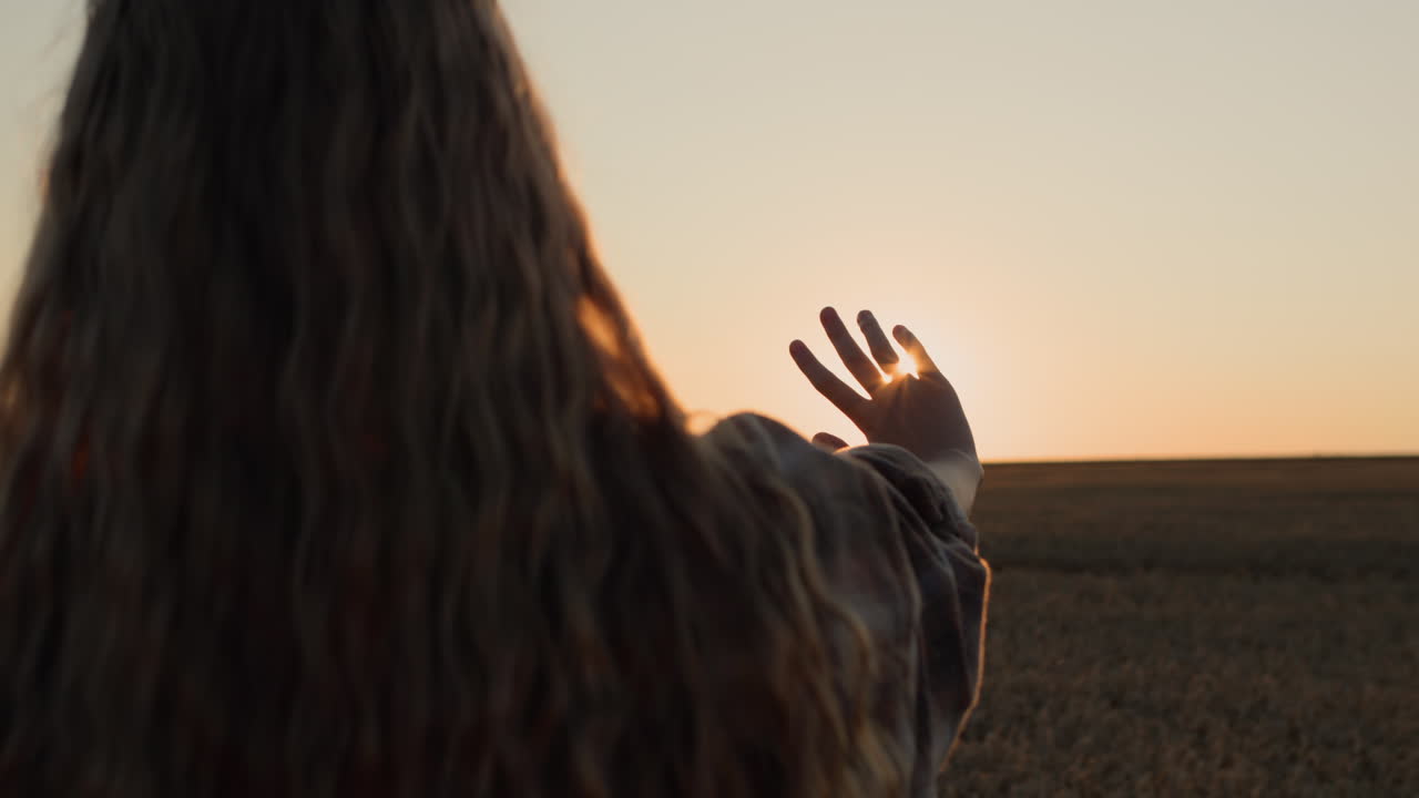 una chica linda con el pelo largo y hermoso extiende la mano hacia el sol poniente.