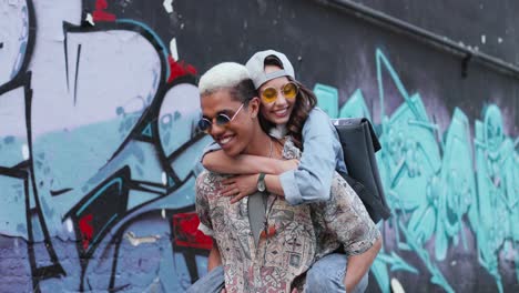 young boy giving her girlfriend a piggyback and walking near a graffity wall in the street