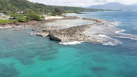 Imágenes-Aéreas-Frente-A-La-Costa-De-La-Isla-Tropical-De-Hawaii-Con-La-Cala-De-Los-Tiburones-Con-Mucha-Costa-Rocosa-Y-Agua-Azul-Clara-Del-Océano-Verde-Esmeralda-En-La-Costa-Con-Bosques-Tropicales