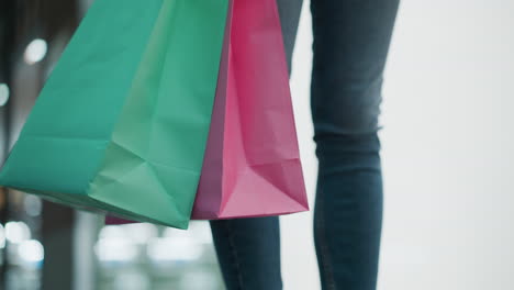 partial view of woman standing with mint and pink shopping bags gently swaying, wearing casual white long-sleeve top and fitted jeans