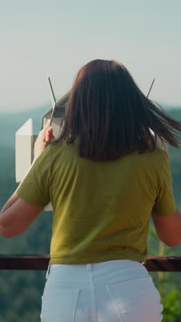 woman uses viewing binoculars at mountain height to take in spectacular view of surrounding hills. unforgettable emotions from memories gained on vacation slow motion