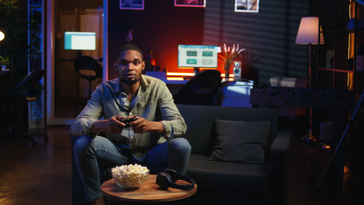 Vertikal video: Afroamerikansk man tillbringar fritiden med att spela tv-spel och äta popcorn.