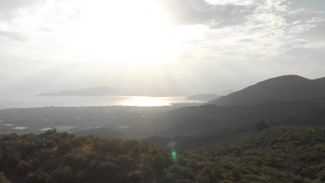 aerial  day drone shot of amazing mountain landscape  green tall trees small traditional village sun shines behind white clouds sun reflects in the sea at background amazing view aegean sea