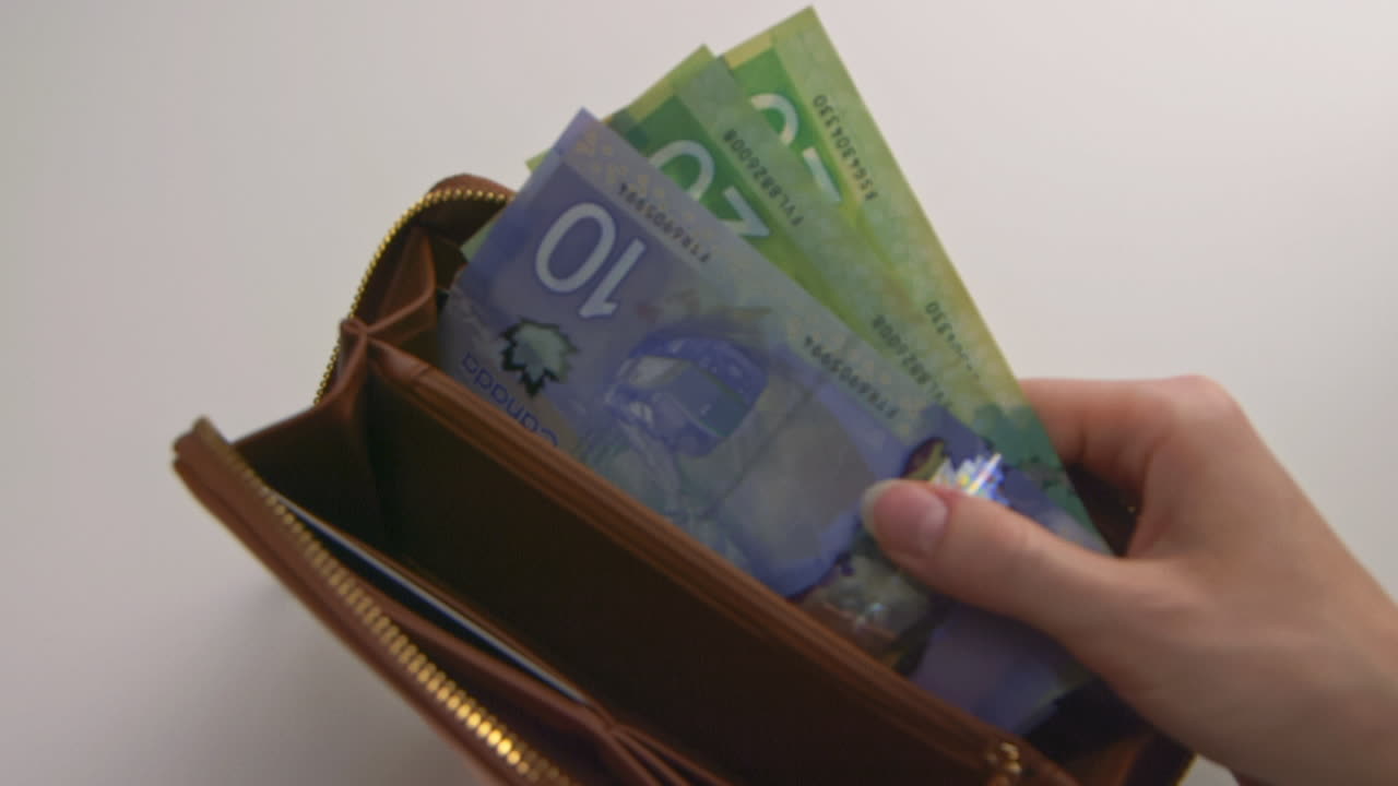 A caucasian woman's hands opening a brown wallet and showing two $20 CDN bills and one $10 CDN bill