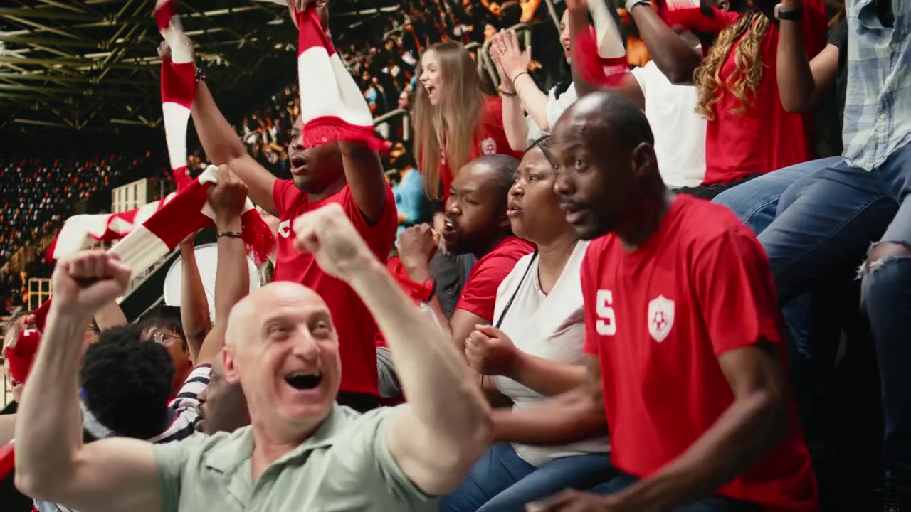 Aficionados de fútbol eufóricos animando y agitando bufandas después de un gol dramático.