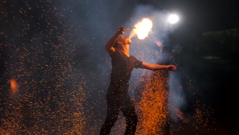 muchas chispas ardientes vuelan en diferentes direcciones. el hombre está respirando una llama enorme. el fuego escapa de la boca. cámara lenta. 4k