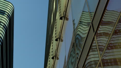 Close-up,-angled-view-of-a-building's-reflective-glass-facade,-showing-the-distorted-reflection-of-another-building-and-the-sky