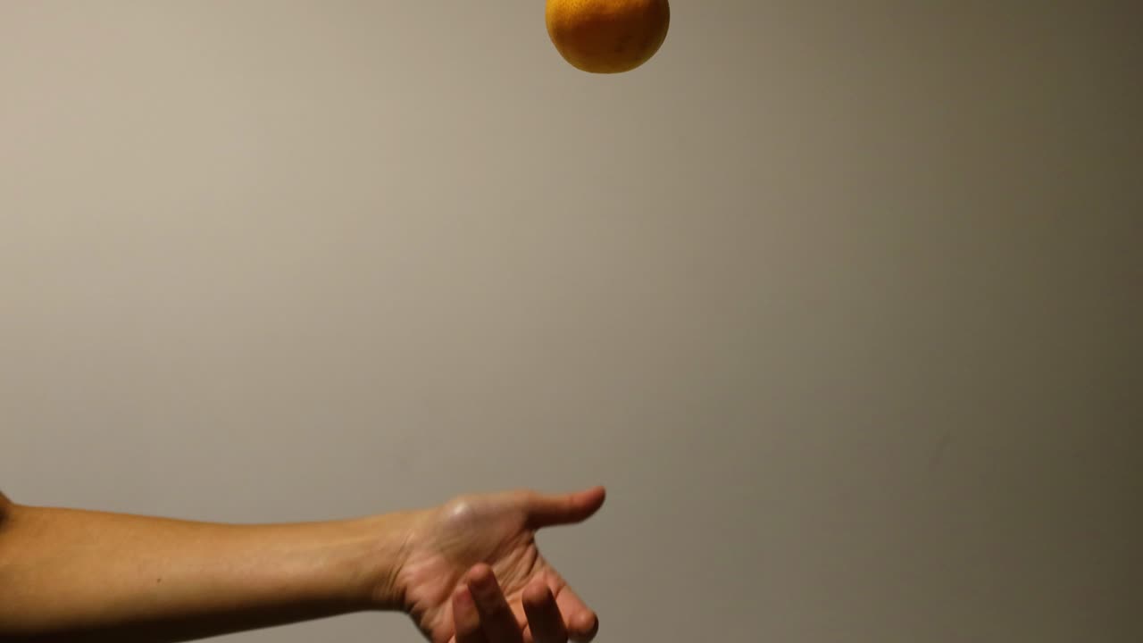A hand throws and catches an orange